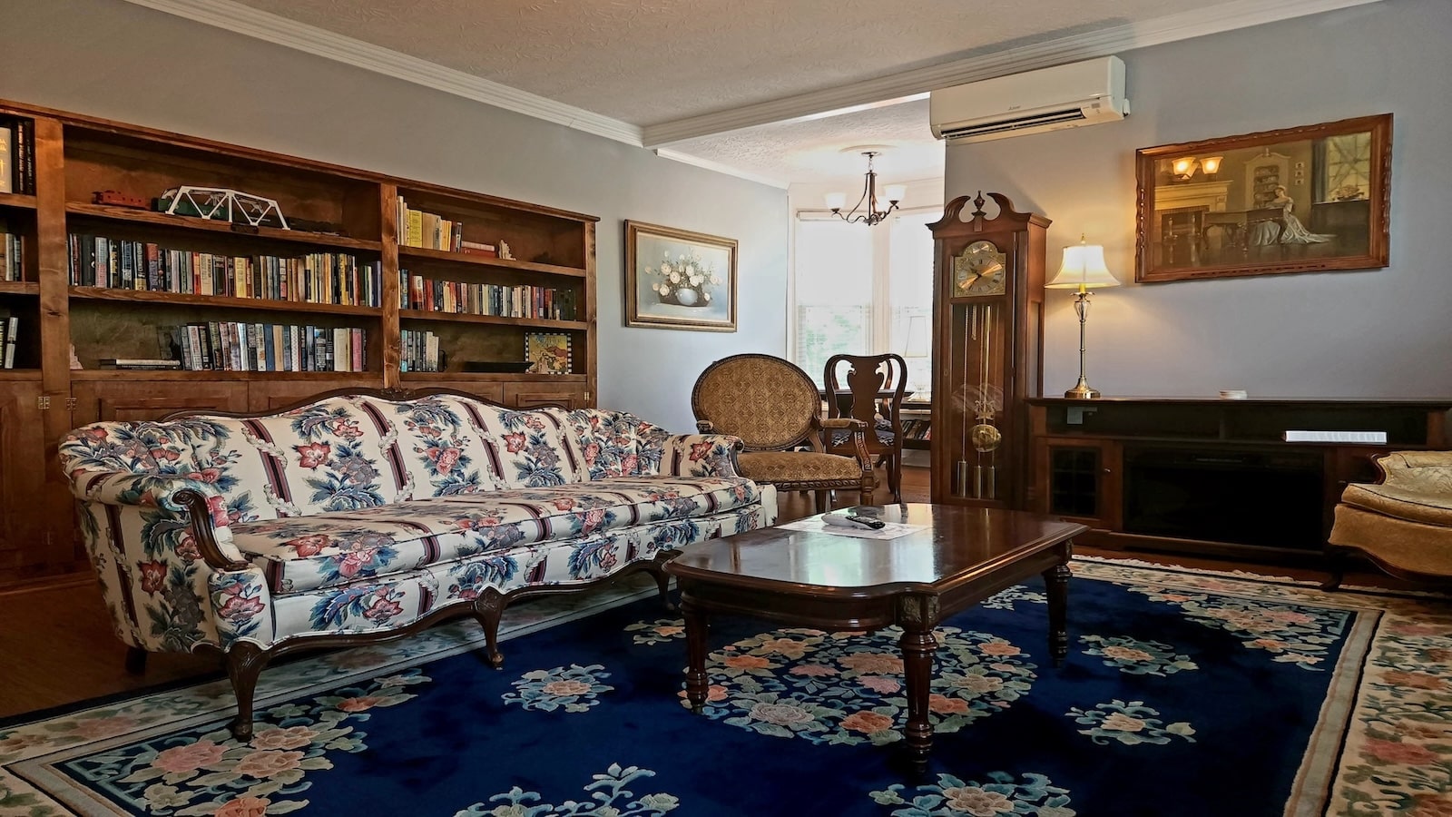 Library with long couch, bookshelves and coffee table with area rug, grandfather clock