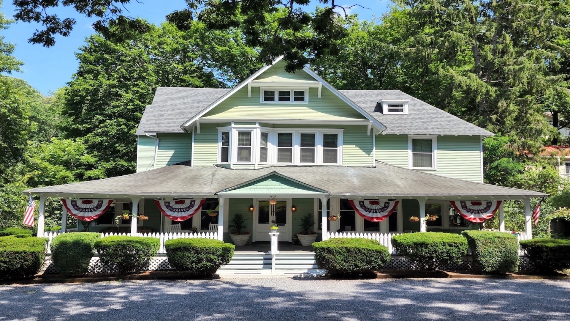 Three-story green house with covered porch and white rocking chairs, bushes in front