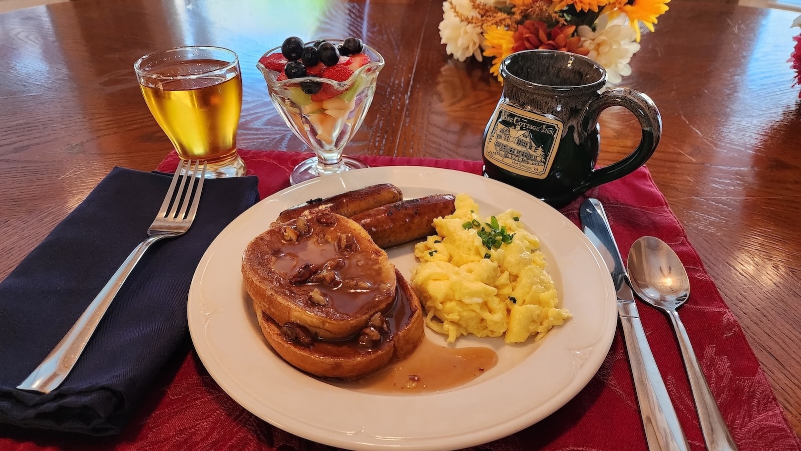 White plate with french toast, sausage and eggs with fruit cup