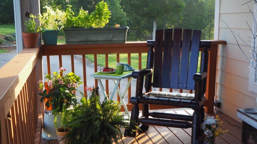 Dark wooden rocking chair on porch surrounded by green potted plants