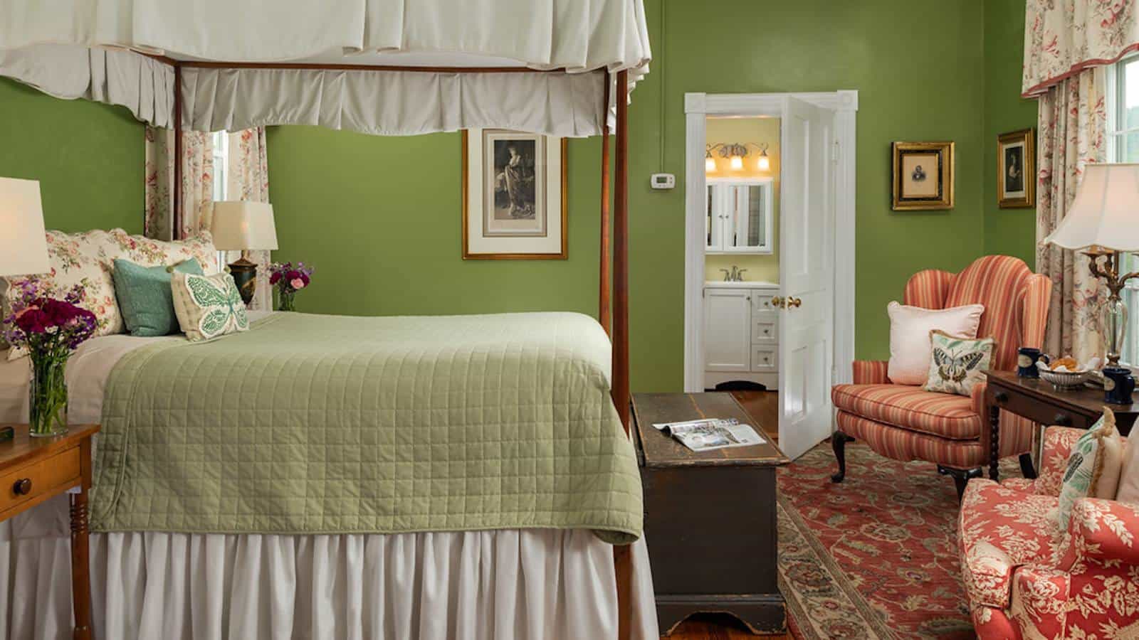 Bedroom with green walls, hardwood flooring, four poster bed with canopy and green blanket, and sitting area