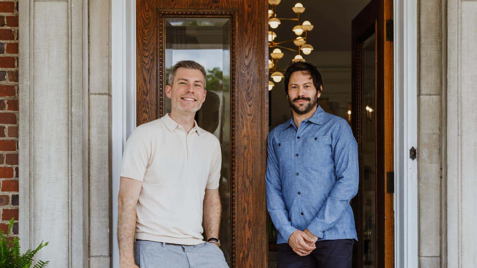 Man with cream shirt and man with blue shirt smiling and standing at the front door of the property