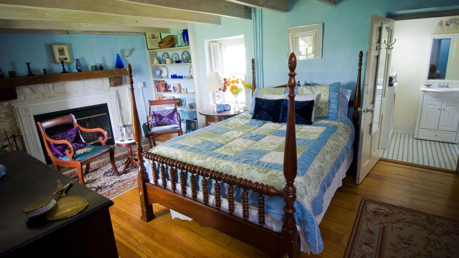 Bedroom with light blue walls, hardwood flooring, dark wooden four poster bed, fireplace, and sitting area