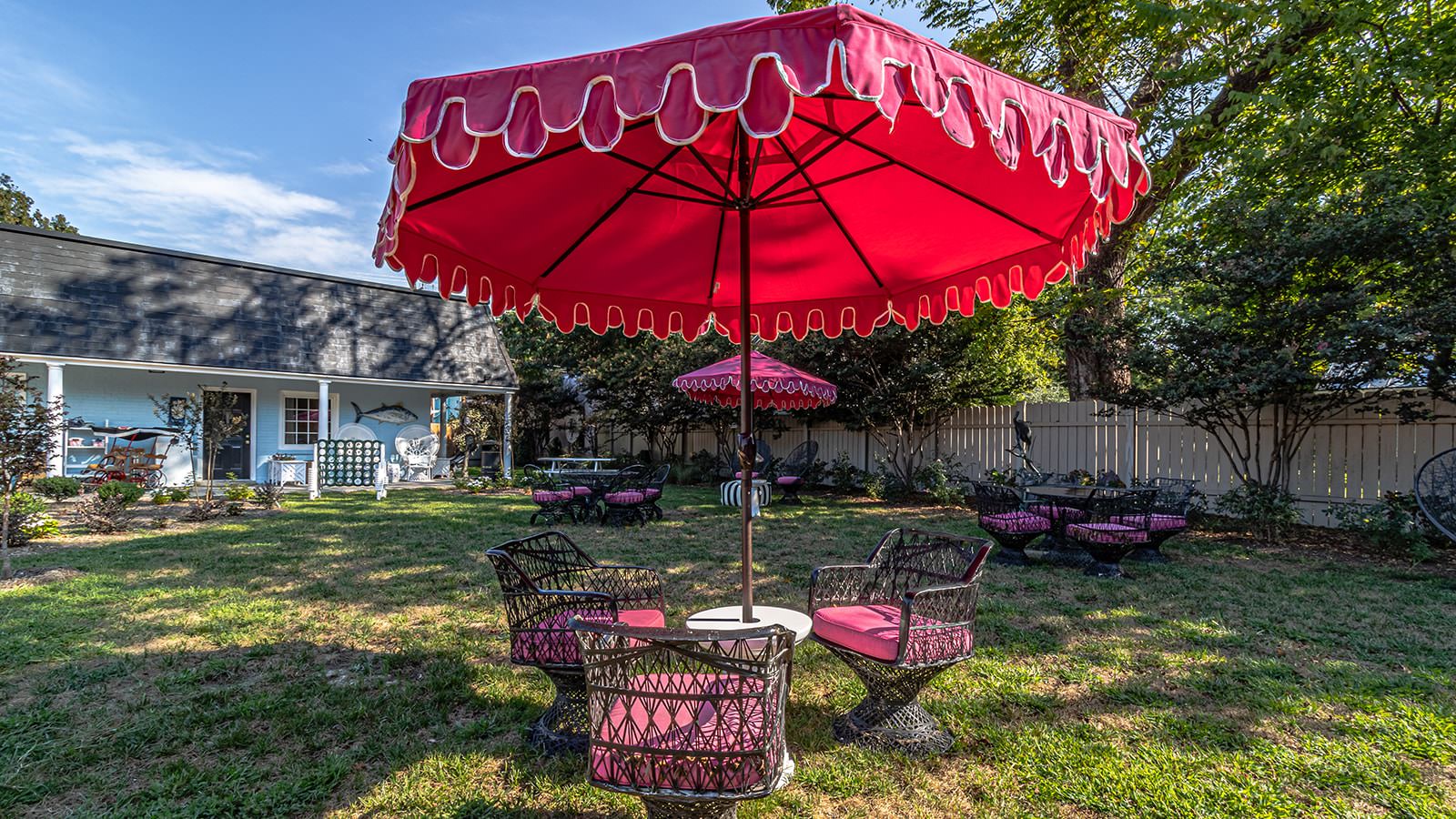 Large backyard with green grass and multiple wrought iron tables and chairs with red umbrellas