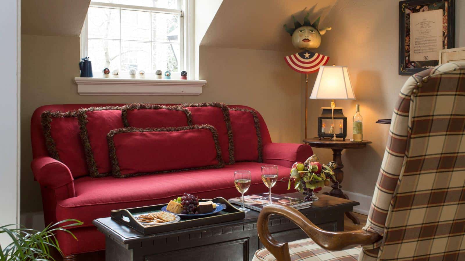 Sitting area with red upholstered sofa, dark wooden trunk as a table, and wooden tray on trunk with fruit, cheese, and crackers