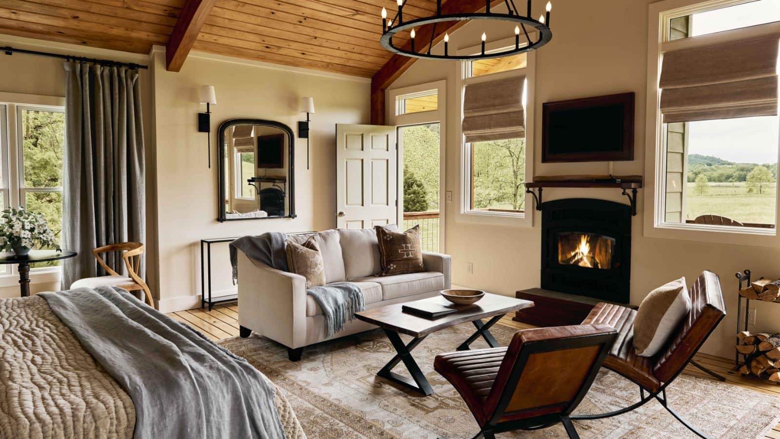 Bedroom with white walls, wooden flooring, wooden ceiling, fireplace, sitting area, and door to patio