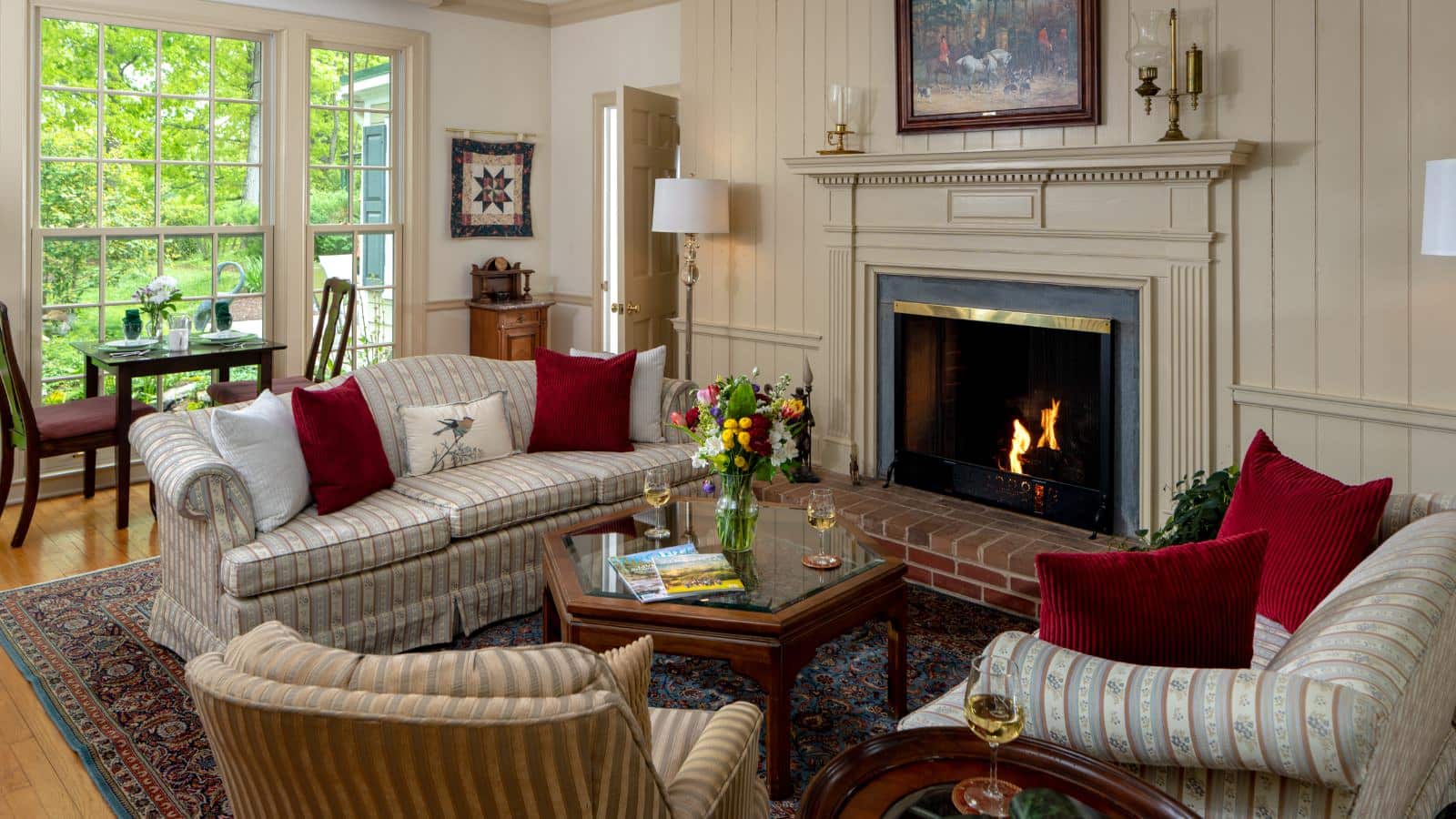 Living room with cream colored, paneled walls, hardwood flooring, fireplace, upholstered sofa, loveseat, and chair, and glass and wood coffee table