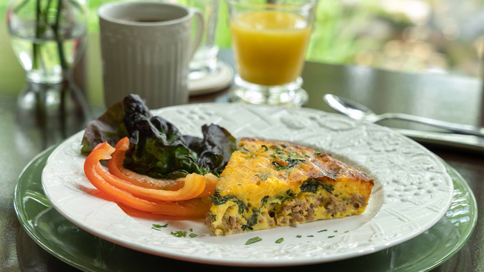 Close up view of a white plate with quiche and sliced red bell pepper