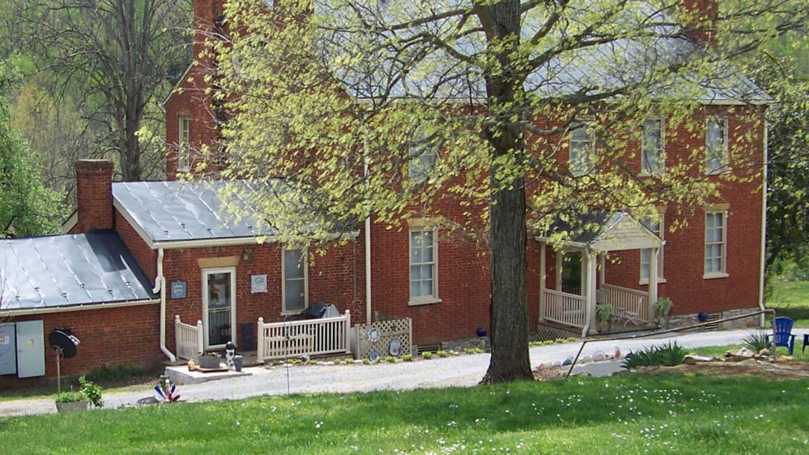 Exterior view of property with red brick and white trim surrounded by green grass and trees