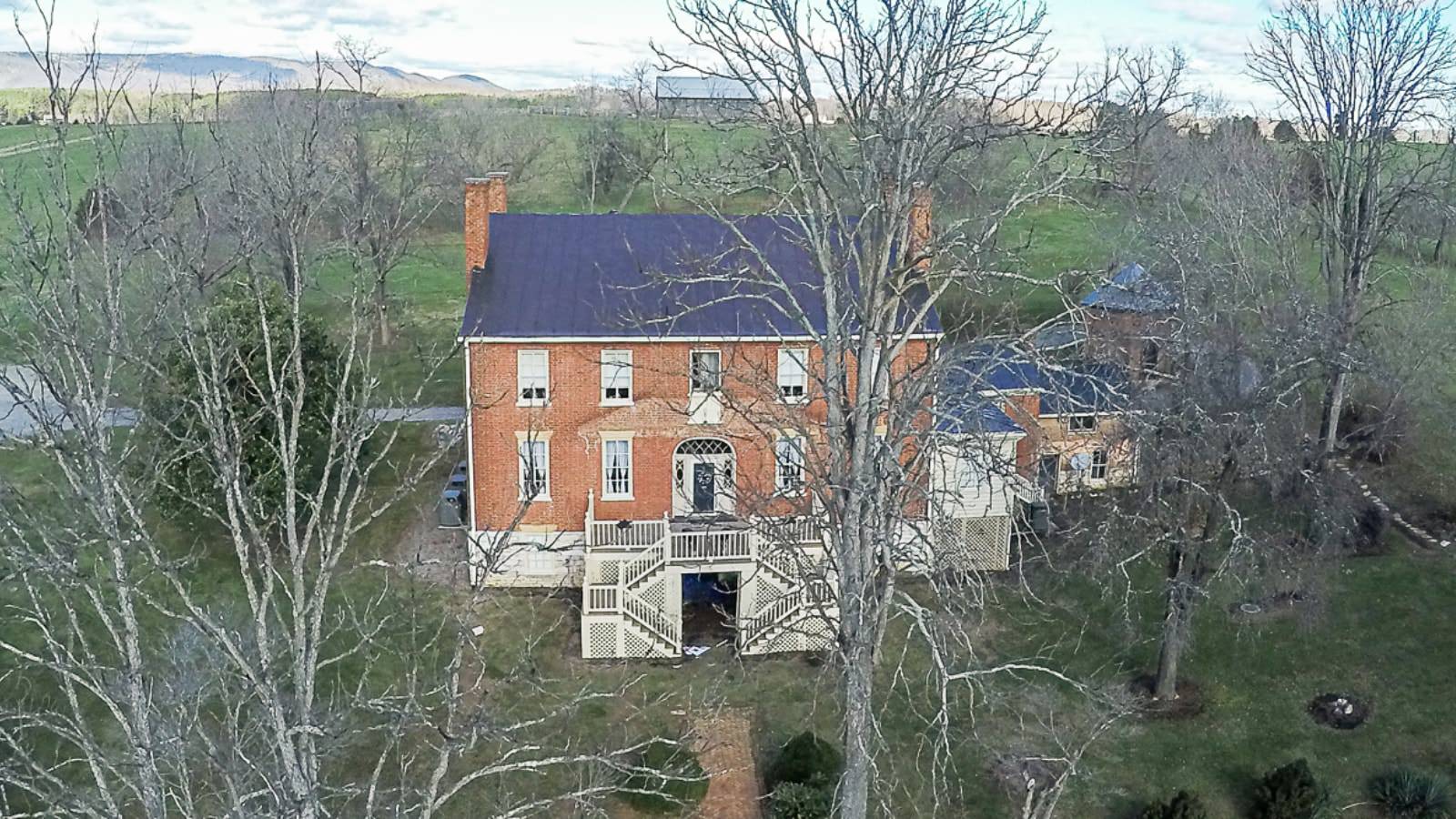 Exterior view of property with red brick and white trim surrounded by green grass and trees