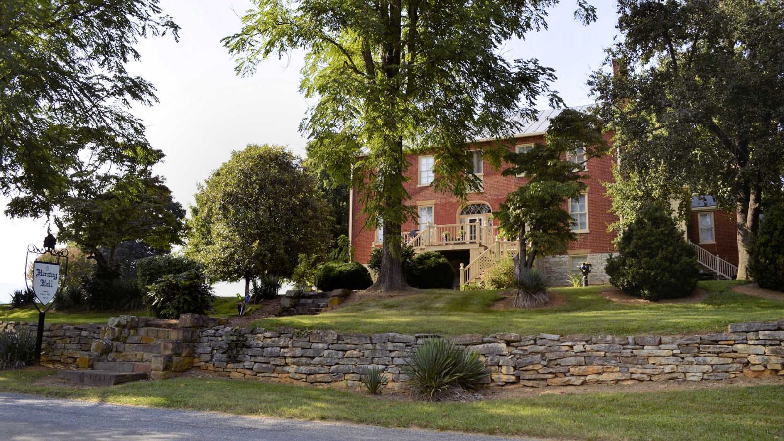 Exterior view of property with red brick and white trim surrounded by green grass and trees