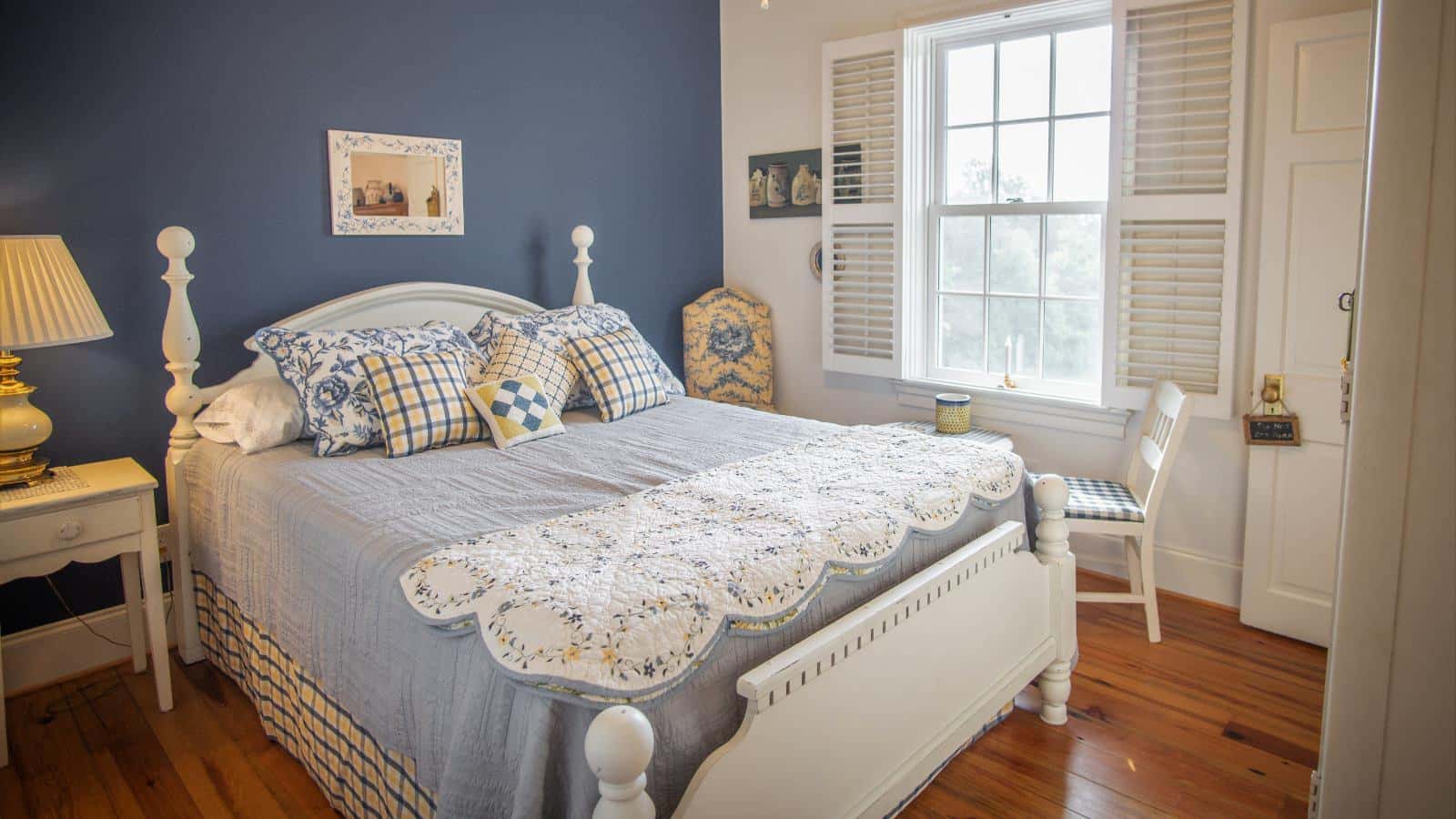 Bedroom with blue and white walls, hardwood flooring, white wooden bed, light blue bedding, white wooden nightstand, and sitting area