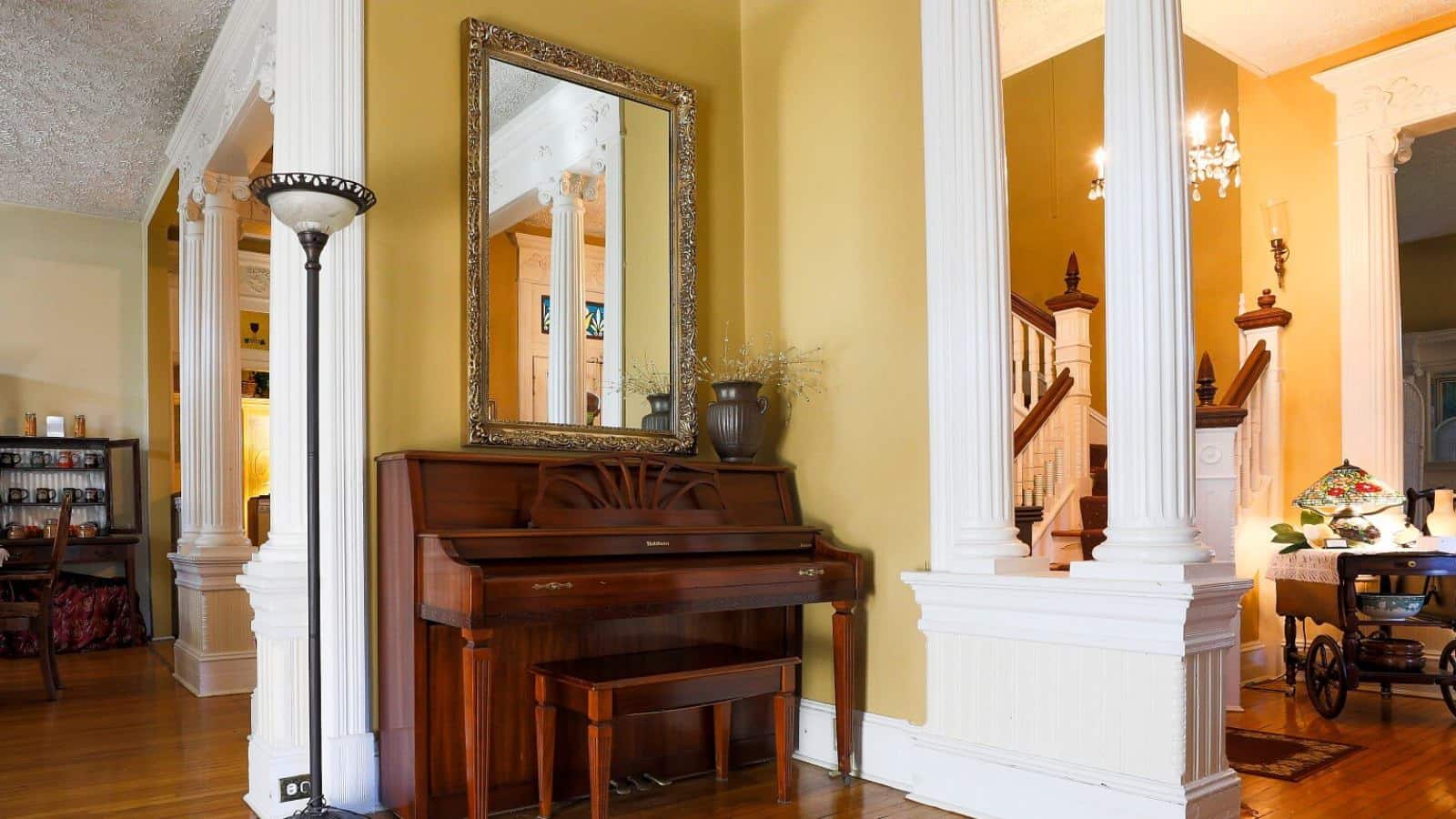 Front entry and living room with yellow walls, hardwood flooring, dark wooden upright piano, and white spindle staircase with dark wooden rails