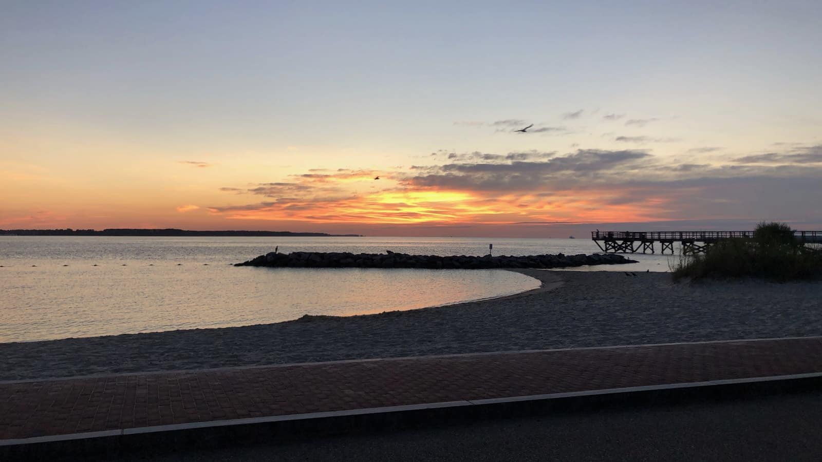 Sandy beach with long boardwalk next to calm water at dusk