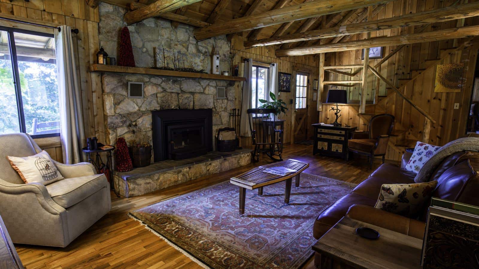 Living room with wooden paneling, hardwood flooring, wooden ceiling, stone brick fireplace, leather sofa, and upholstered armchair