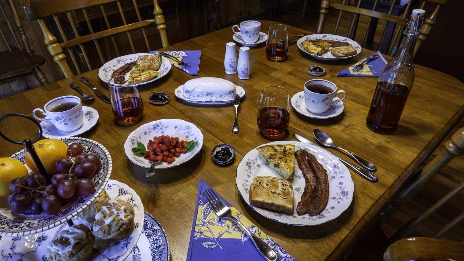 Wooden dining table and chairs with three place settings with breakfast dishes and bowls of fruit