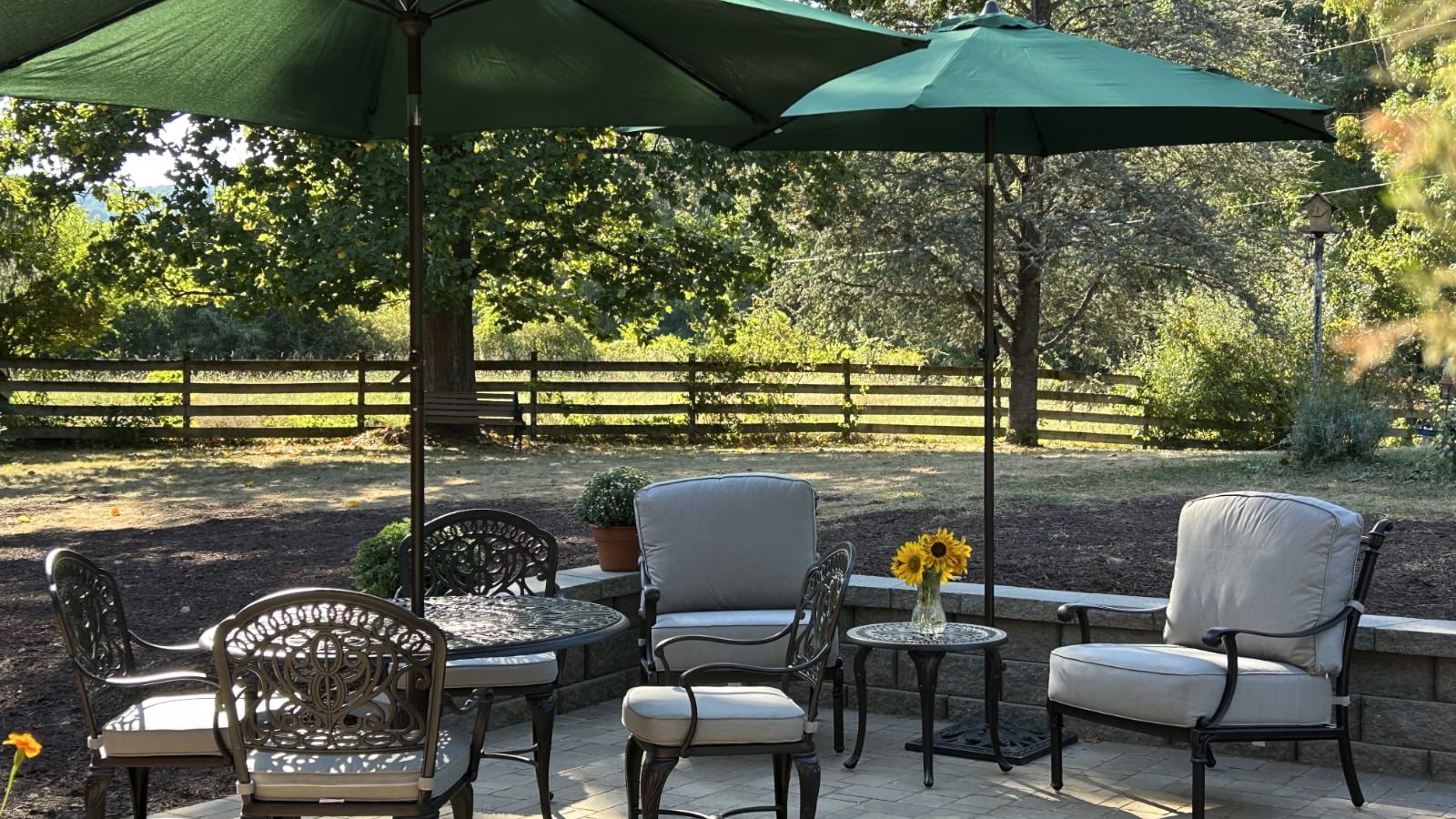 Paver patio with patio furniture and two green umbrellas with green trees in the background