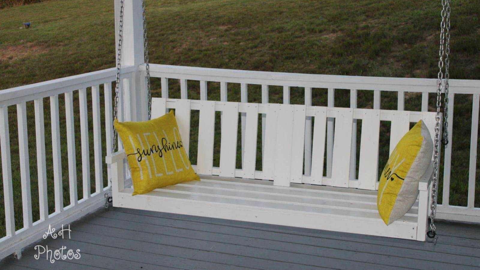 White wooden porch swing with two yellow pillows that say Hello Sunshine