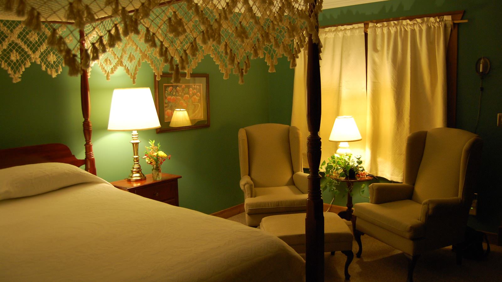 Bedroom with dark green walls, carpeting, four poster bed with canopy and white bedding, and sitting area
