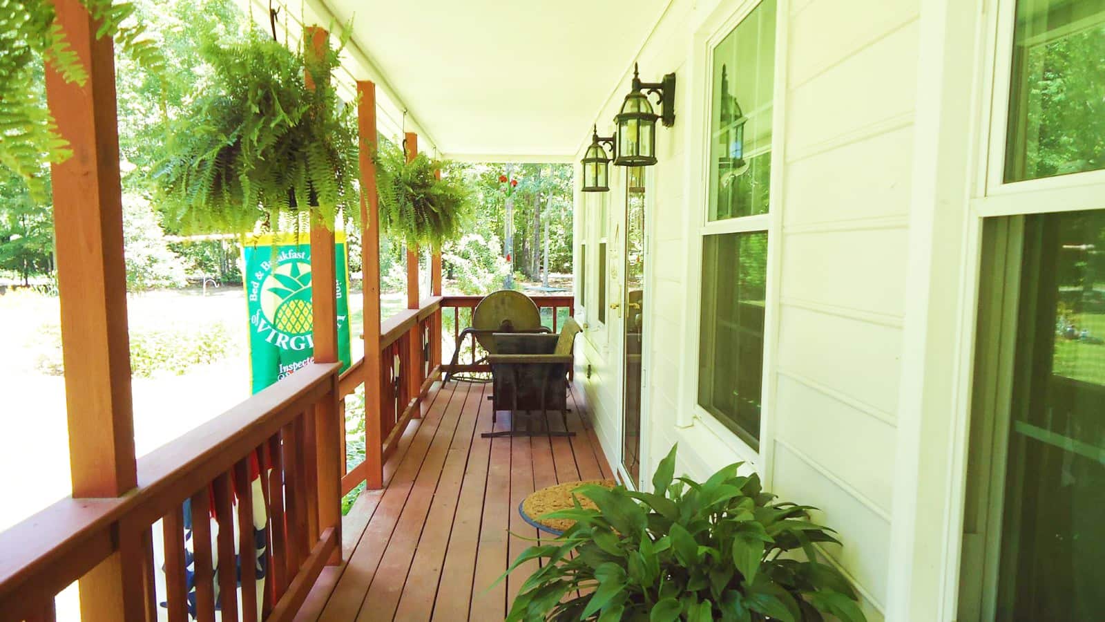Wooden front porch of property with a patio chair, potted plant, and hanging fern plants