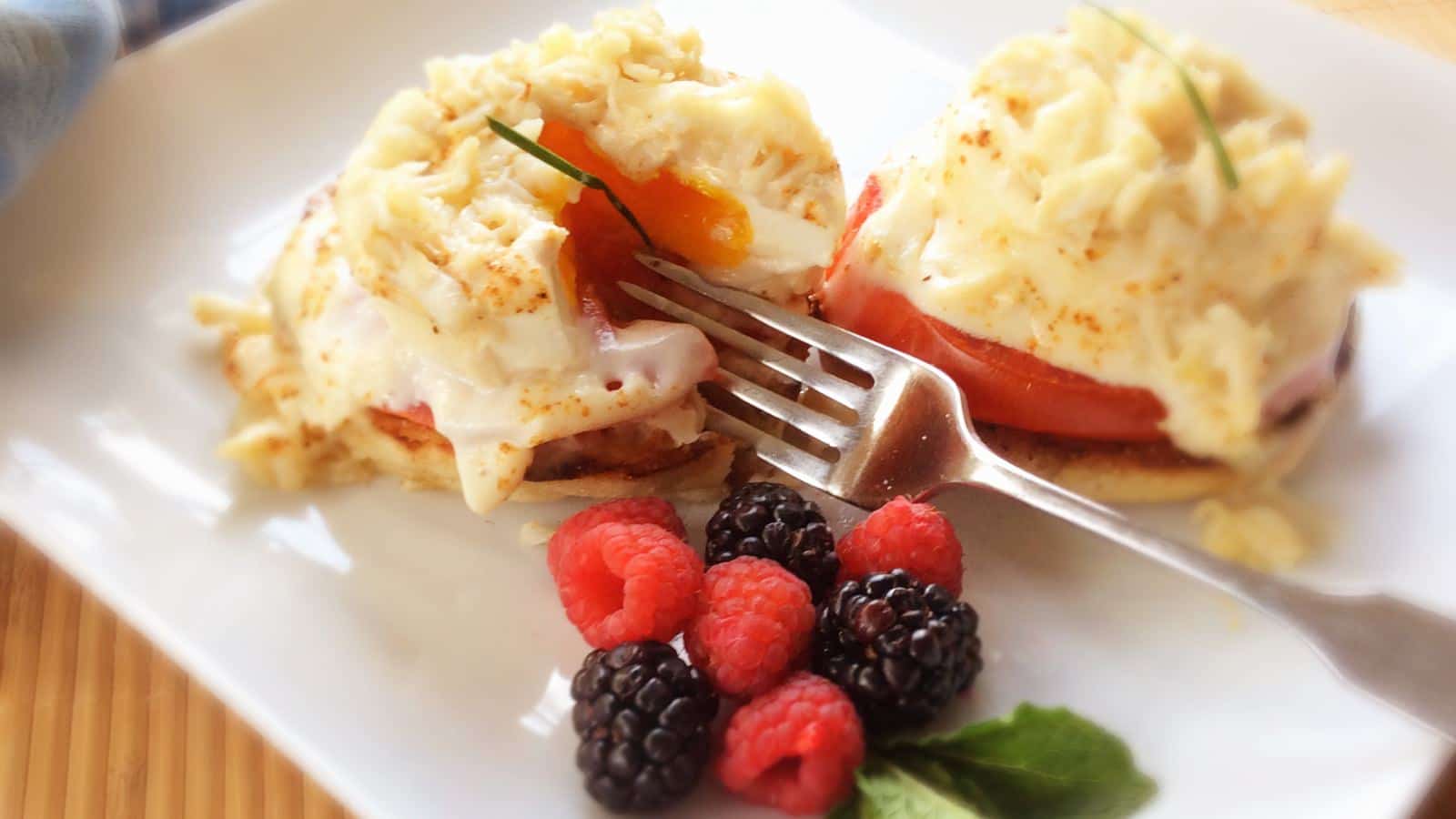 Close up view of eggs benedict, raspberries, and blackberries on a white plate