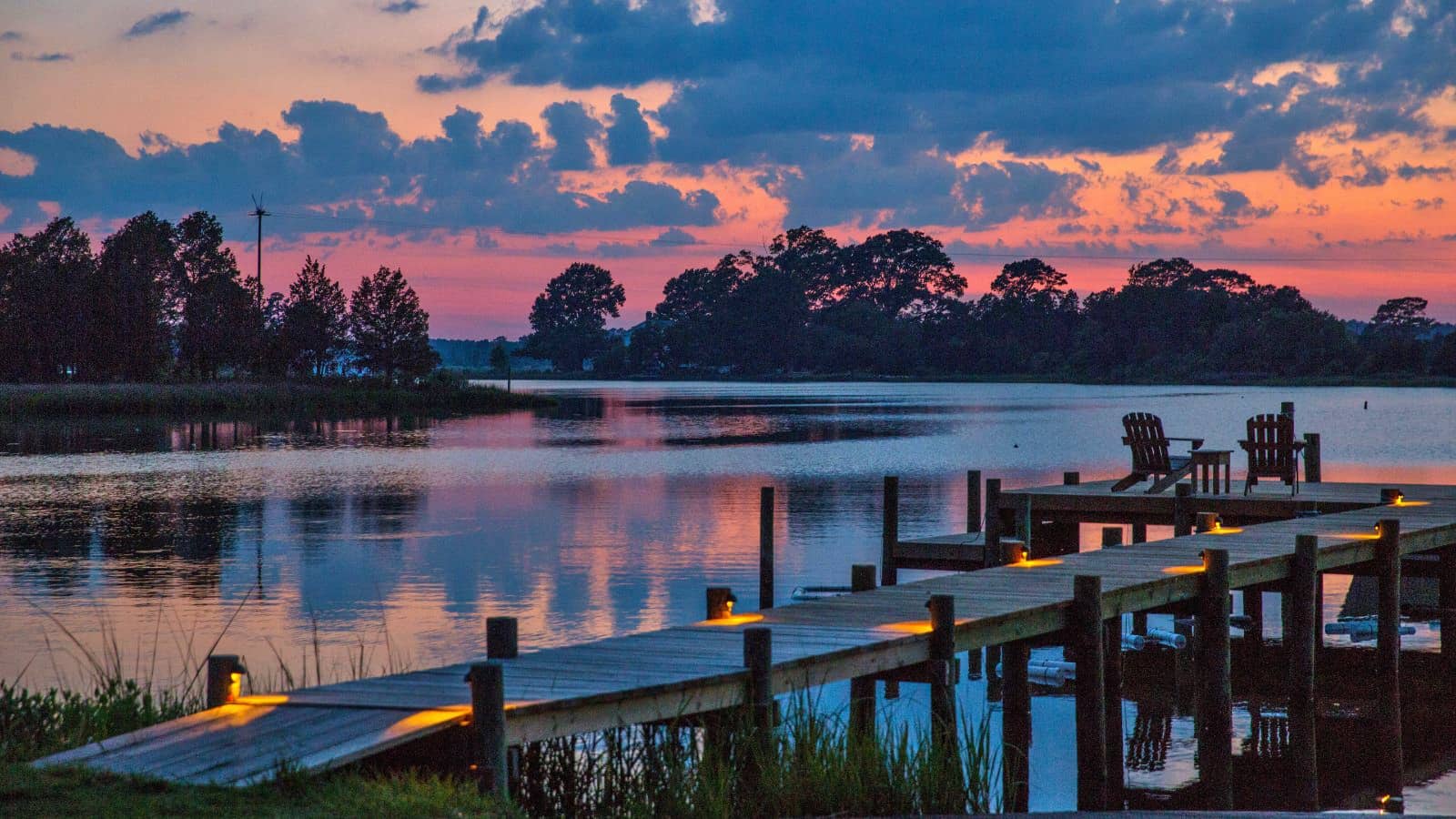 Wooden dock and pier surrounded by calm water with trees in the background at dusk