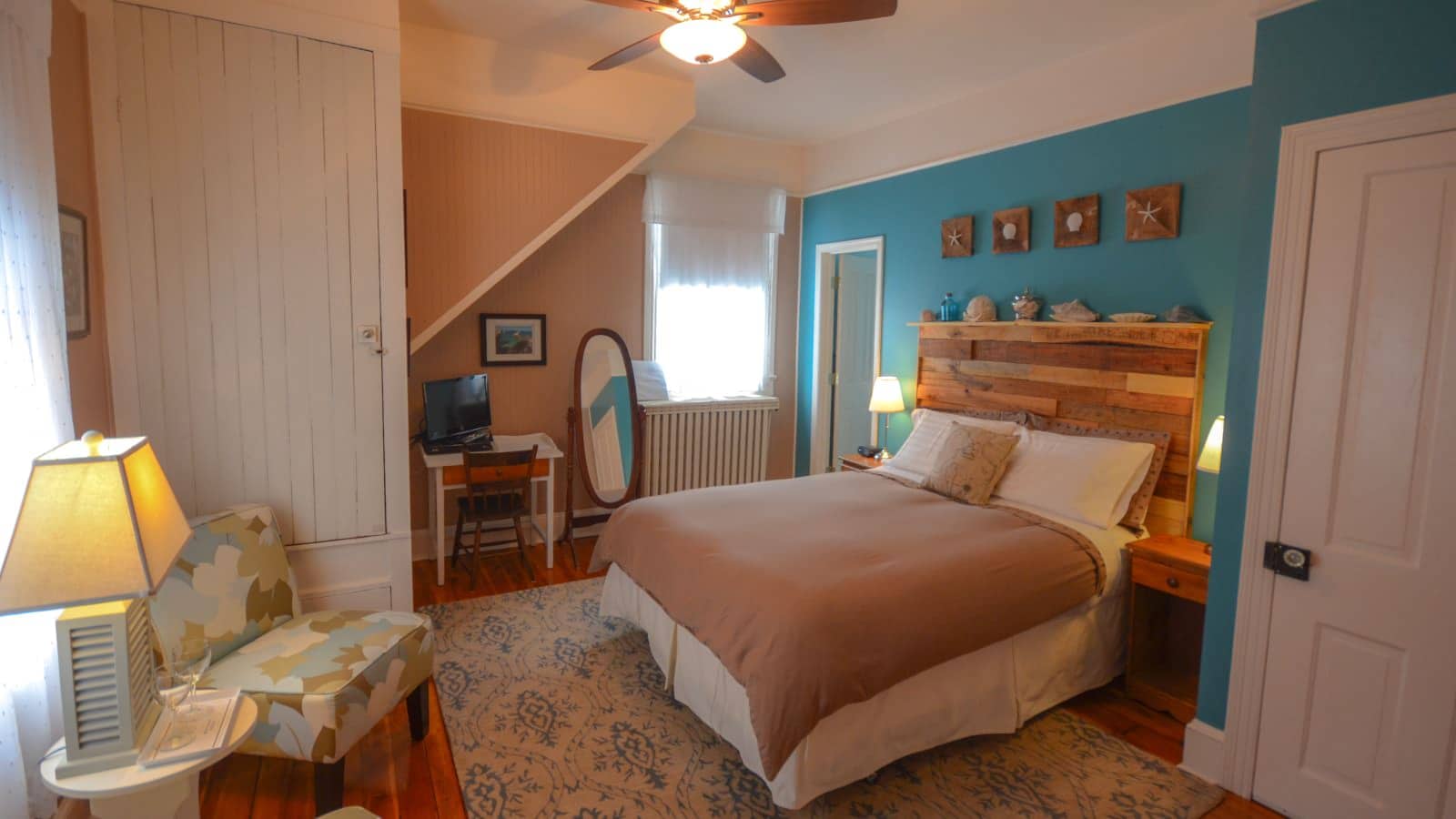 Bedroom with turquoise and tan walls, hardwood flooring, wooden bed, white and brown bedding, small desk, and a sitting area