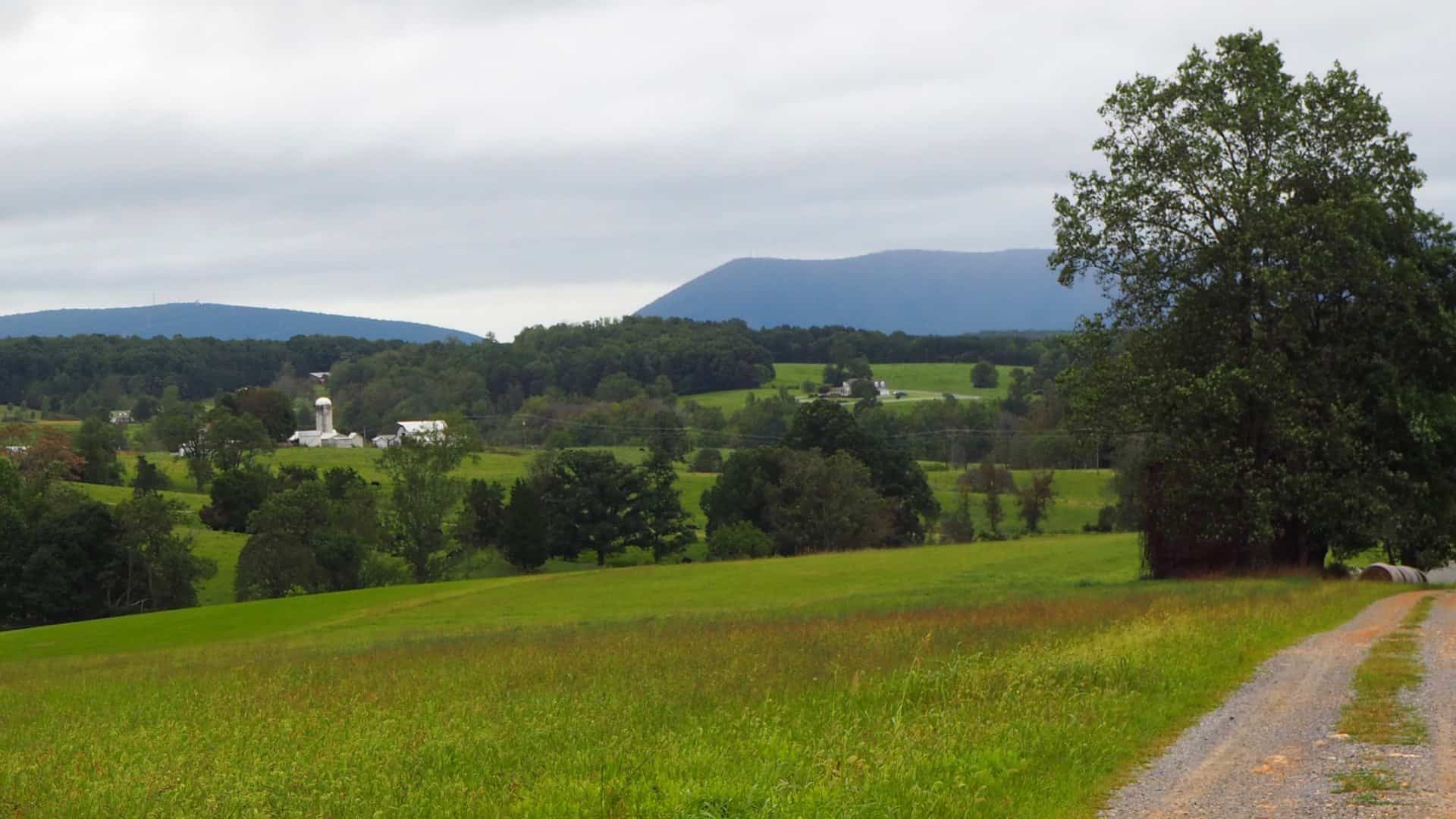 Countryside with green grass, trees, farms, and hills in the background