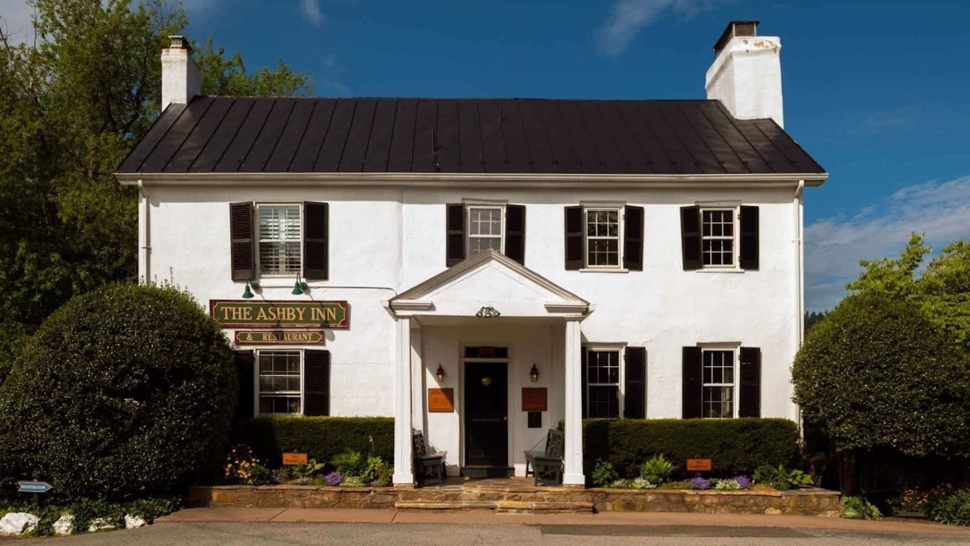 Exterior view of property painted white with black shutters and surrounded by green shrubs, bushes, and trees