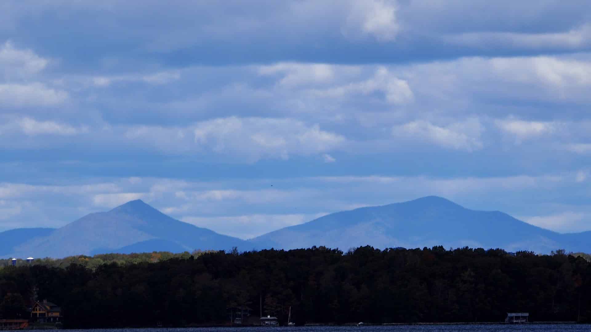 Large green trees with blue ridge mountains in the background with many clouds in the sky