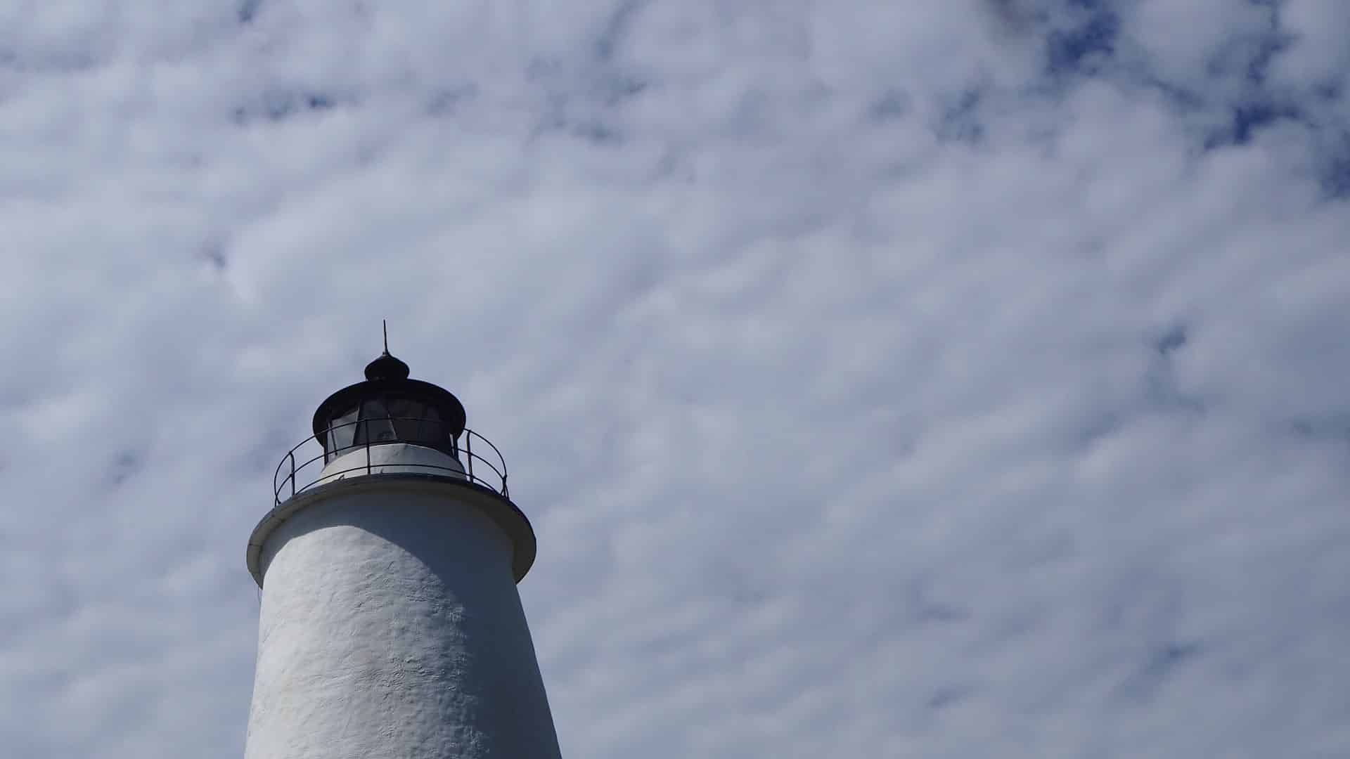 Top of white lighthouse with white clouds in the background
