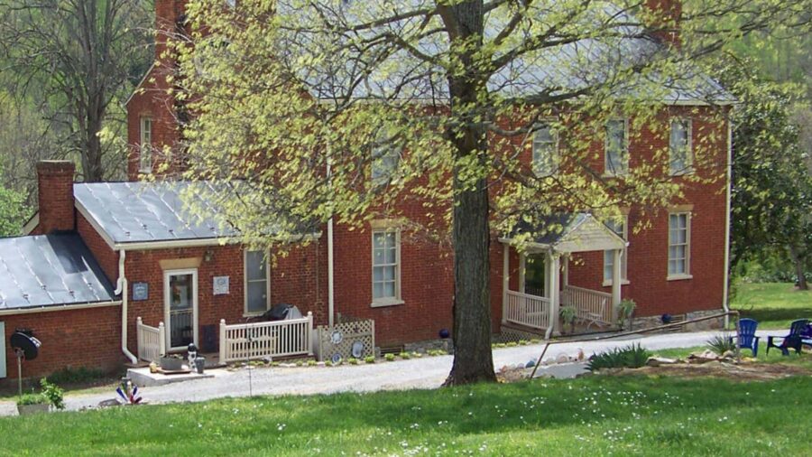 Exterior view of property with red brick and white trim surrounded by green grass and trees