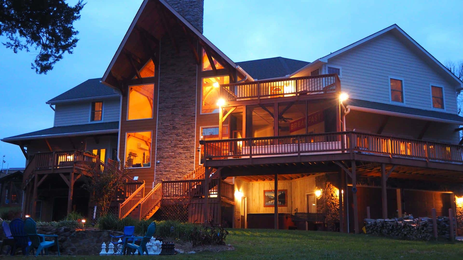 Exterior view of a three level property with large stone fireplace all lighted up at dusk