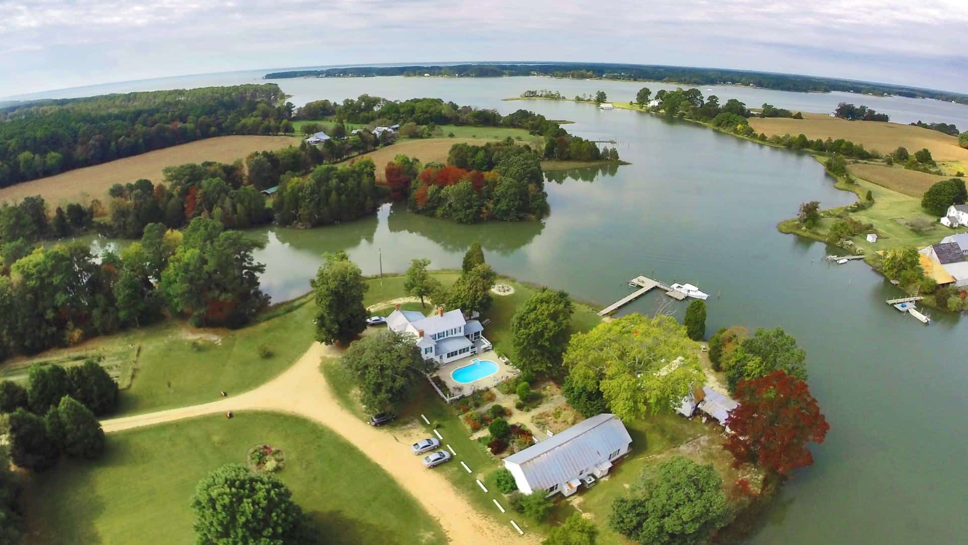 Aerial view of the property surrounded by green grass, trees, and water