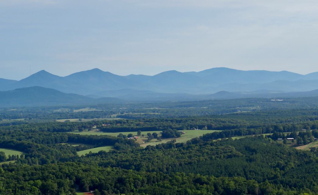 Aerial view of green trees, rolling hills, and mountains in the background