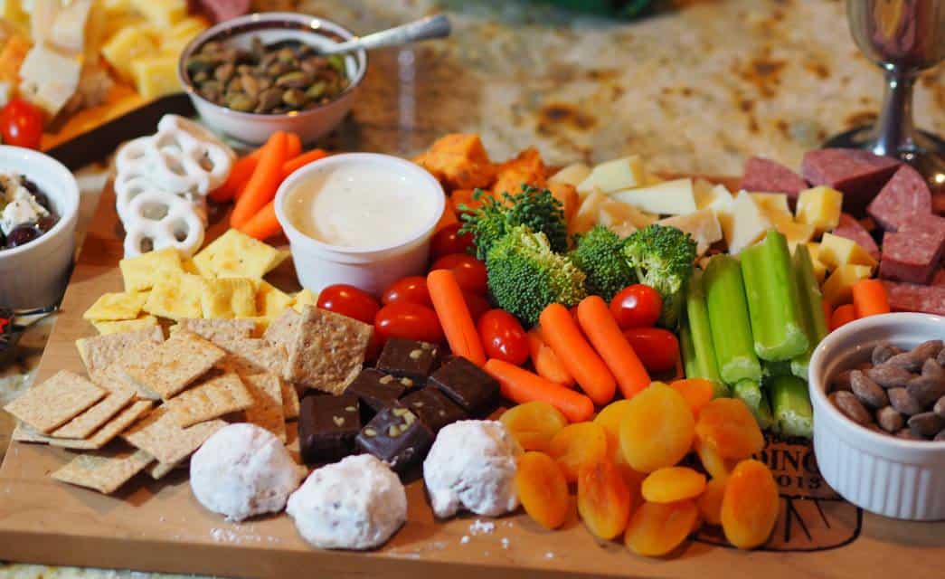 Charcuterie board full of crackers, sweets, nuts, veggies, cheeses, meats and dip