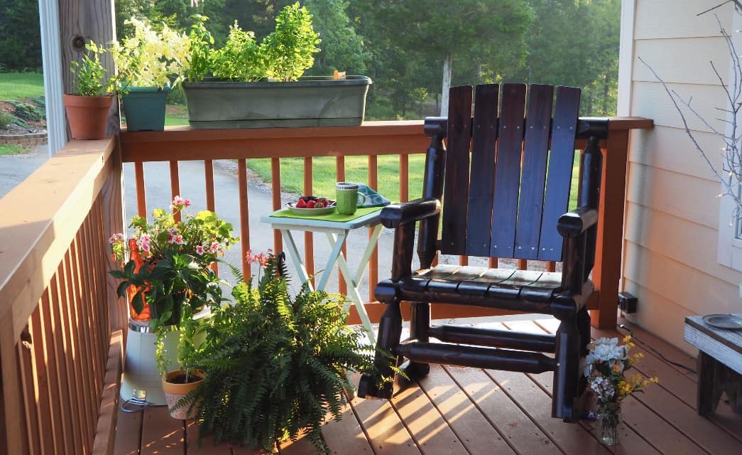 Dark wooden rocking chair on porch surrounded by green potted plants